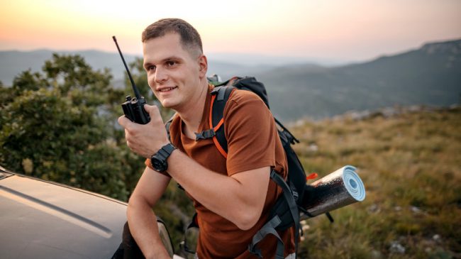 Hiker talking on radio while resting in mountains Best Walkie Talkies for Hiking